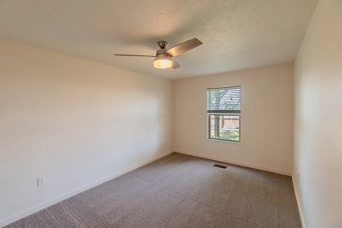 Large bedroom with neutral carpet, ceiling fan, and natural light&mdash;ideal for cozy living in a Battlefield, MO rental.