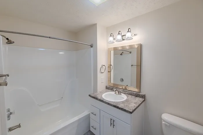 Modern bathroom with a white bathtub and shower combo, brushed nickel fixtures, updated lighting, and a faux granite countertop vanity in a Battlefield apartment.