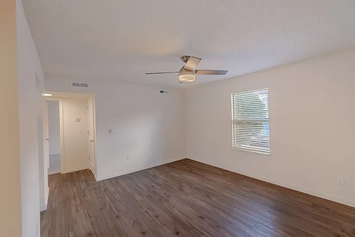 Spacious living room at Huntley Ridge East apartments in Springfield, MO, with wood-style flooring, ceiling fan, and natural light from a large window.