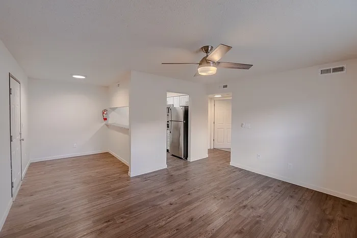 Open-concept living and dining space at Huntley Ridge East, showcasing wood-look flooring, neutral walls, ceiling fan, and a view into the kitchen with stainless steel appliances.