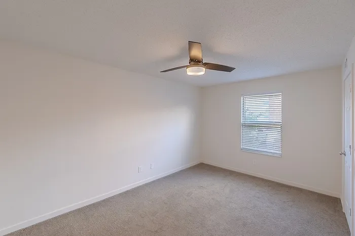 Bright bedroom at Huntley Ridge East with soft carpet flooring, ceiling fan, and large window bringing in natural light.