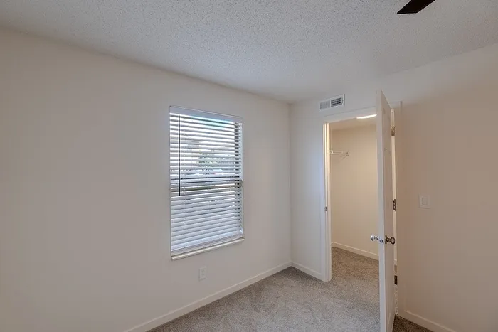 bedroom at Huntley Ridge East in Springfield, MO, with carpet floors, window blinds, and direct access to a walk-in closet.