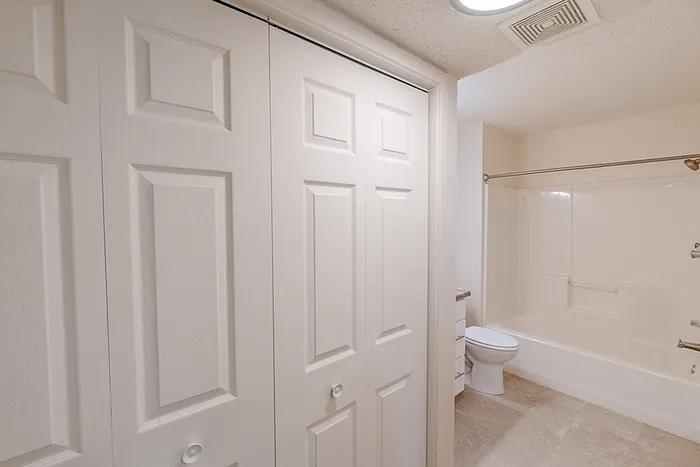 Full bathroom at Huntley Ridge East featuring a white tub and shower combo, toilet, modern vanity, and double-door storage closets.