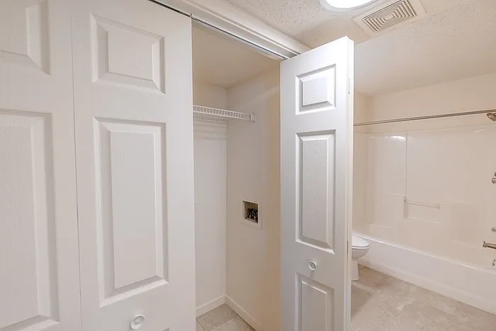 In-unit laundry area at Huntley Ridge East apartments in Springfield, MO, with washer and dryer connections and convenient shelving next to the bathroom.