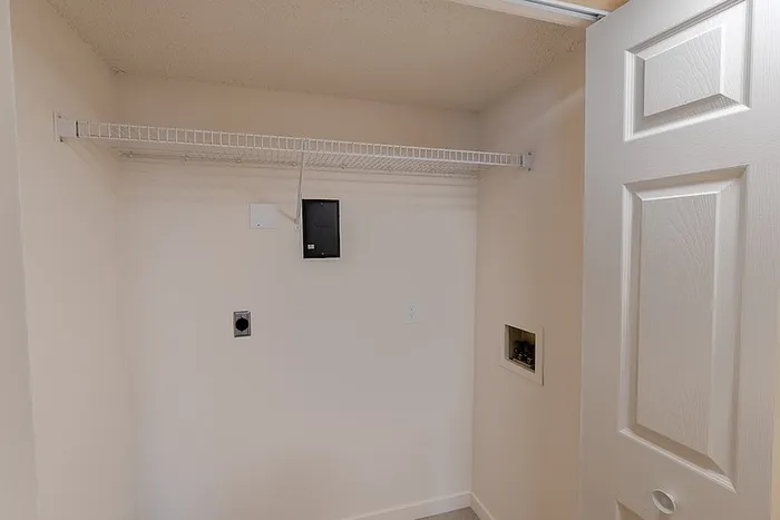 In-unit laundry space at Huntley Ridge East in Springfield, MO, featuring washer and dryer connections with an overhead wire shelf for storage.