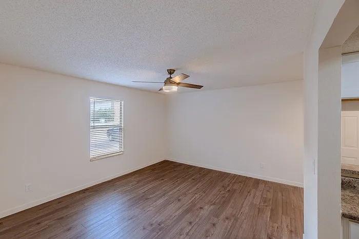 Bright living room at Huntley Ridge East in Springfield, MO, showcasing wood-style flooring, ceiling fan with light, and large window bringing in natural light.