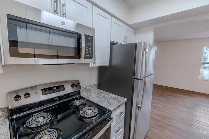 Modern kitchen at Huntley Ridge East in Springfield, MO, with stainless steel appliances including an electric stove, over-the-range microwave, and refrigerator, accented by white cabinetry and granite-style countertops.