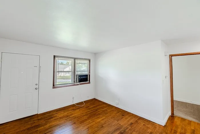 Bright living room at Village Club Apartments in Springfield, MO, featuring hardwood floors, white walls, and a large window with natural light.
