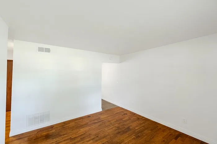 Spacious living area at Village Club Apartments in Springfield, MO, with hardwood floors and a simple, open layout connecting to the hallway.