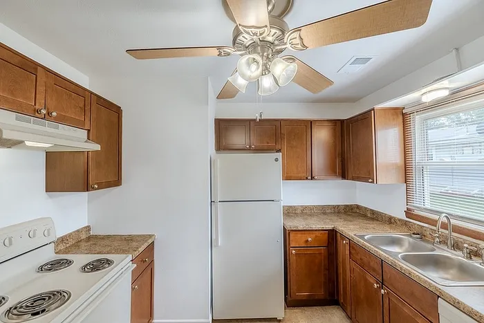 Kitchen at Village Club Apartments in Springfield, MO, with wood cabinetry, marble-style countertops, white appliances, and a ceiling fan.