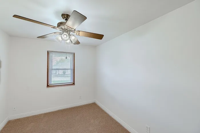 Bedroom at Village Club Apartments in Springfield, MO, with soft carpeting, a ceiling fan, and a window letting in natural light.