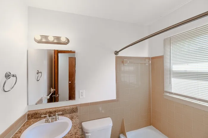 Bathroom at Village Club Apartments in Springfield, MO, featuring a full shower and tub combo, beige tile surround, and a vanity with granite-style countertop.