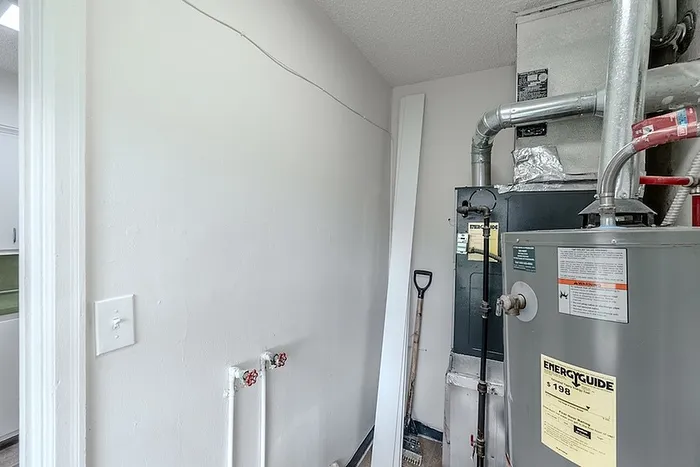 Utility room at Village Club Apartments in Springfield, MO, showing the water heater, HVAC system, and washer hookups with bright white walls.