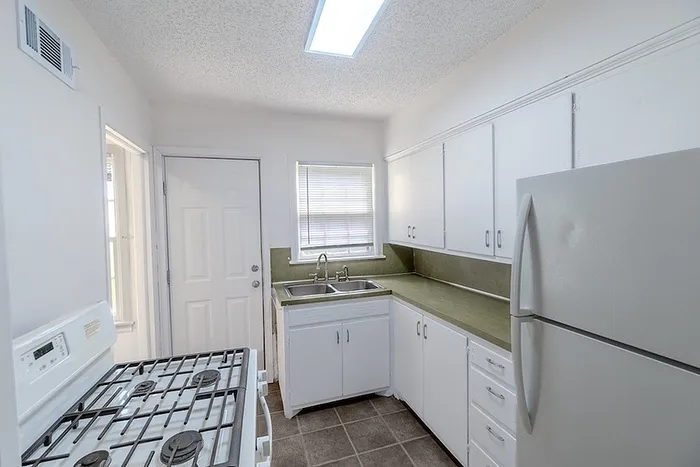 Kitchen at Village Club Apartments in Springfield, MO, featuring white cabinetry, green countertops, a gas stove, and full-size refrigerator with window light.