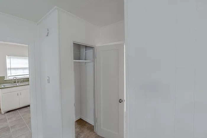 Living room storage view at Village Club Apartments in Springfield, MO, with white trim and doors connecting to the kitchen area.