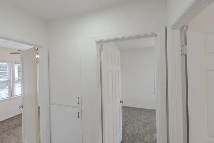 Hallway at Village Club Apartments in Springfield, MO, showing bright white walls, built-in cabinets, and entrances to multiple bedrooms.