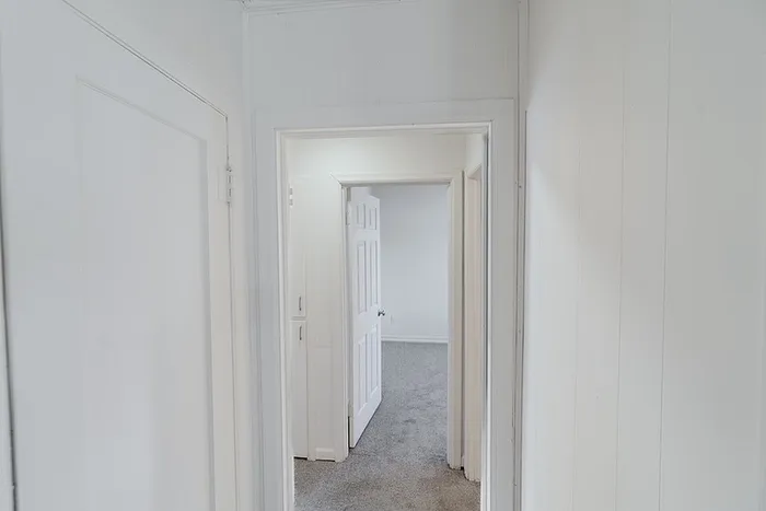 Hallway at Village Club Apartments in Springfield, MO, leading to carpeted bedrooms with white doors and trim.