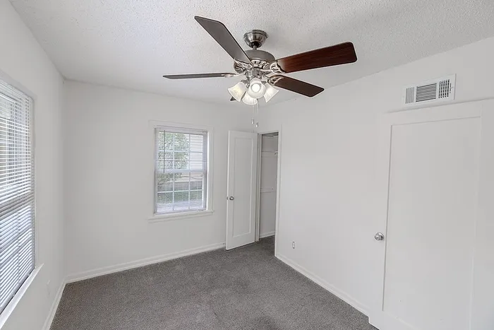 Bedroom with closet at Village Club Apartments in Springfield, MO, featuring gray carpet, white walls, and ceiling fan lighting.