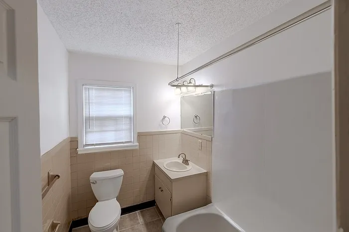 Bathroom at Village Club Apartments in Springfield, MO, with tan tile, a bathtub and shower combo, vanity with mirror, and bright overhead lighting.
