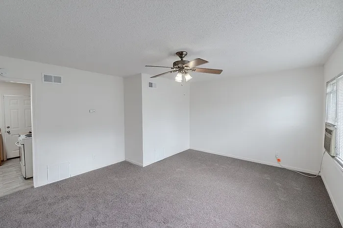 Spacious living room at Village Club Apartments in Springfield, MO, featuring soft gray carpet, ceiling fan lighting, and large windows allowing natural light.