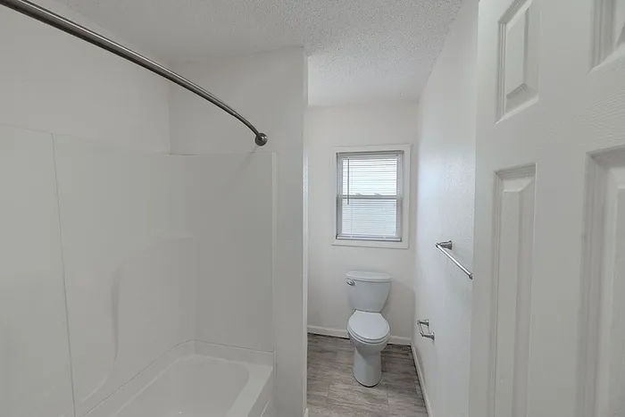 Bathroom at Village Club Apartments in Springfield, MO, with a full bathtub and shower combo, white tile surround, and natural light from the window.