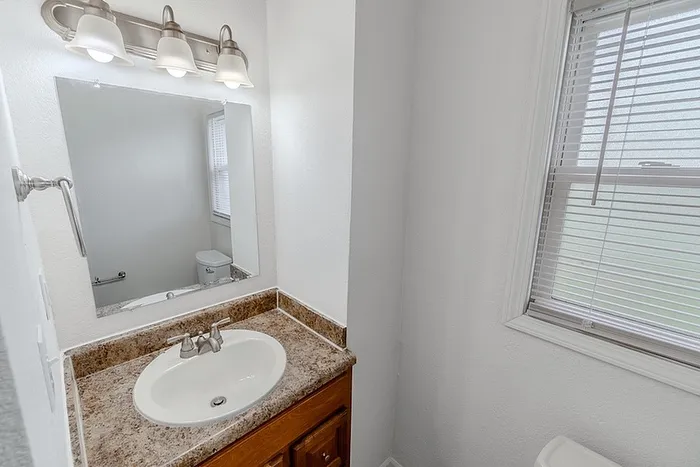 Bathroom vanity at Village Club Apartments in Springfield, MO, featuring a granite-style countertop, large mirror, and updated lighting fixture.