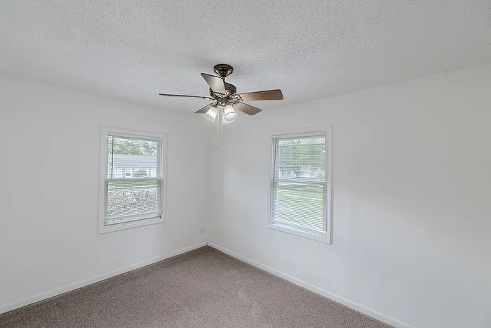 Bedroom at Village Club Apartments in Springfield, MO, with two windows for natural light, soft carpet, and ceiling fan with lighting.