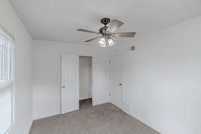 Bedroom with closet at Village Club Apartments in Springfield, MO, featuring white doors, gray carpet, and ceiling fan lighting.