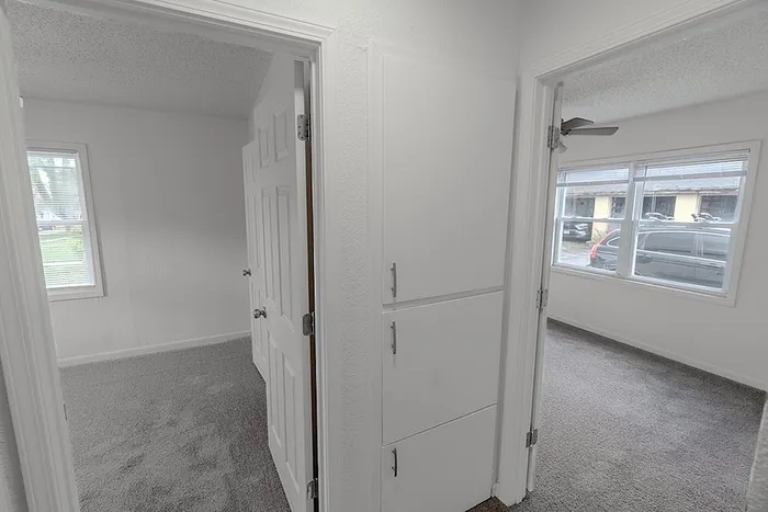 Hallway at Village Club Apartments in Springfield, MO, with built-in storage cabinets and access to two bright bedrooms.