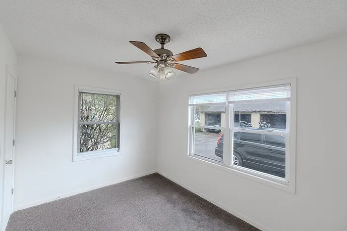 Bedroom at Village Club Apartments in Springfield, MO, with large windows, ceiling fan, and neutral carpet flooring.