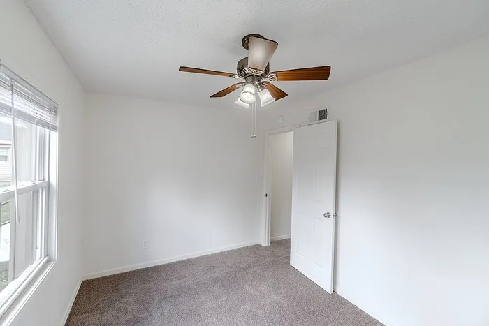 Bedroom at Village Club Apartments in Springfield, MO, showcasing a ceiling fan, white walls, and bright natural light from multiple windows.