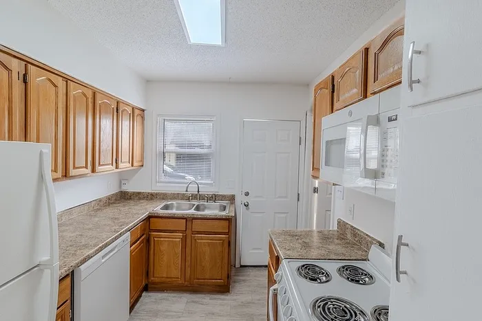Kitchen at Village Club Apartments in Springfield, MO, featuring oak cabinetry, marble-style countertops, white appliances, and a bright skylight above.
