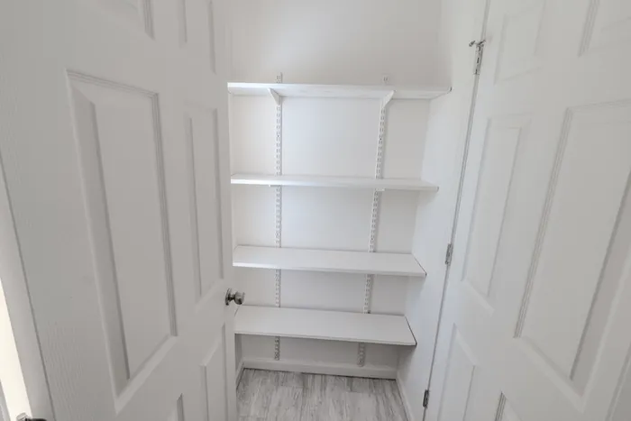 Pantry at Village Club Apartments in Springfield, MO, with built-in white shelving and light gray tile flooring for additional kitchen storage.