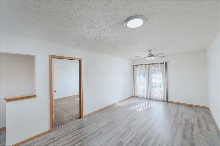 Bright and airy living space with wood-style flooring, ceiling fan, and large glass doors leading to a patio area.