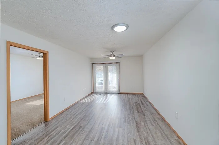 Bright and spacious living area with sleek wooden flooring, modern ceiling fan, and large sliding doors leading to a sunlit outdoor view.