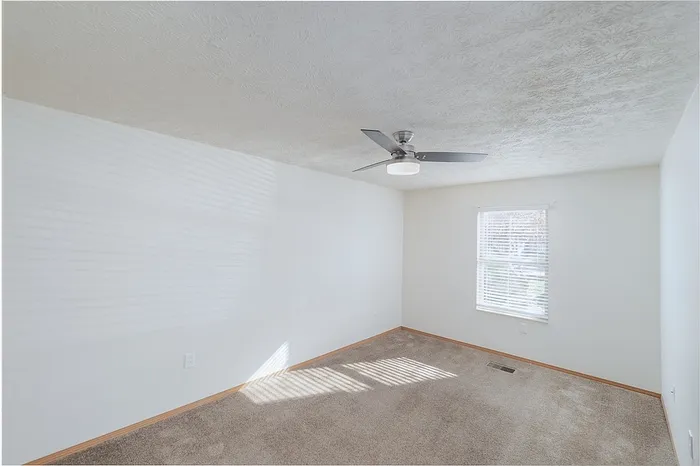 Bright, inviting bedroom with plush carpeting, modern ceiling fan, and large window for natural light.
