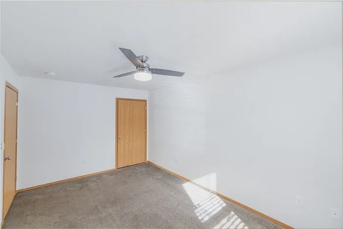 Bright and airy room with plush carpeting, modern ceiling fan, and natural light streaming in, offering a tranquil living space.