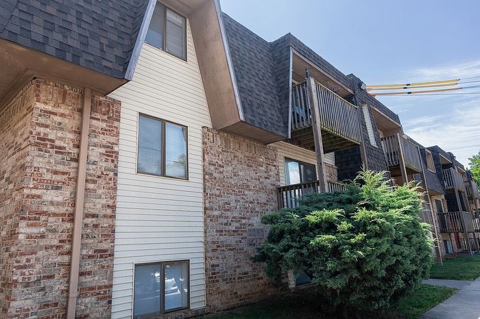 Charming apartment building with rustic brick and siding facade, featuring quaint balconies and lush greenery.
