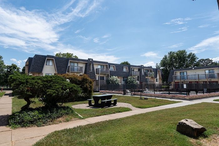 Charming apartment complex with lush green landscaping, cozy balconies, and a refreshing outdoor pool under a clear blue sky.