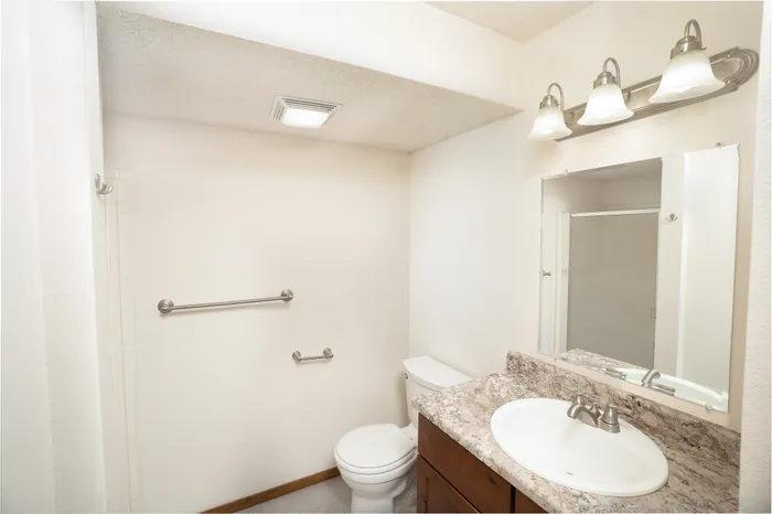 Bathroom vanity area at Catalpa East Apartments in Springfield, Missouri, featuring a sink with countertop, mirror, toilet, wall-mounted towel bar, and overhead lighting.