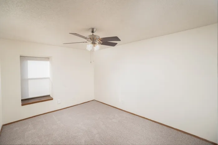 bedroom at Catalpa East Apartments in Springfield, Missouri, showing carpeted floors, neutral wall color, ceiling fan with light fixture, and a window providing natural light.