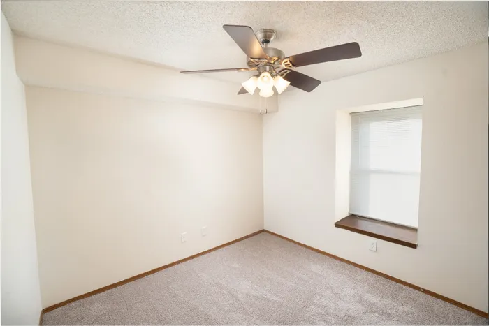 Bedroom at Catalpa East Apartments in Springfield, Missouri, with carpeted flooring, neutral walls, ceiling fan with light, and a window providing natural light.