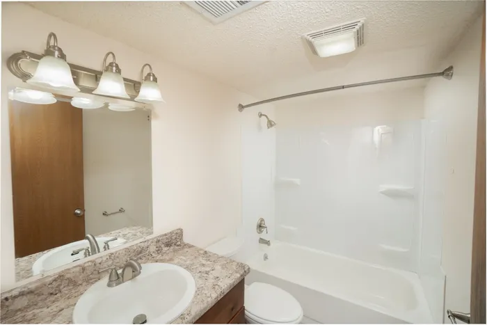 Bathroom at Catalpa East Apartments in Springfield, MO, featuring a tub and shower combination, vanity with sink, large mirror, and overhead lighting.