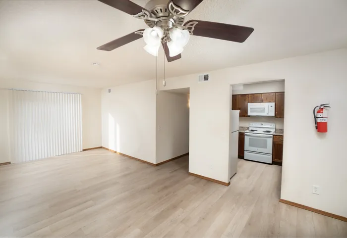 Open living and dining area at Catalpa East Apartments in Springfield, Missouri, showcasing light wood-style flooring, a ceiling fan, and a partial view of the kitchen entrance.