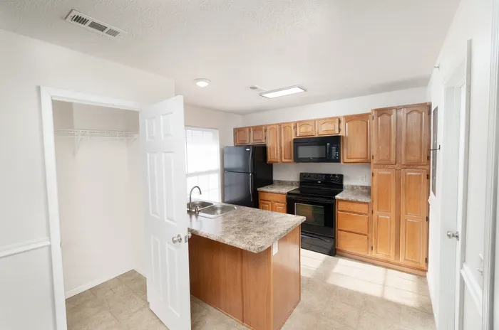 Inviting kitchen with warm wooden cabinetry, sleek black appliances, and granite countertops, perfect for modern living.