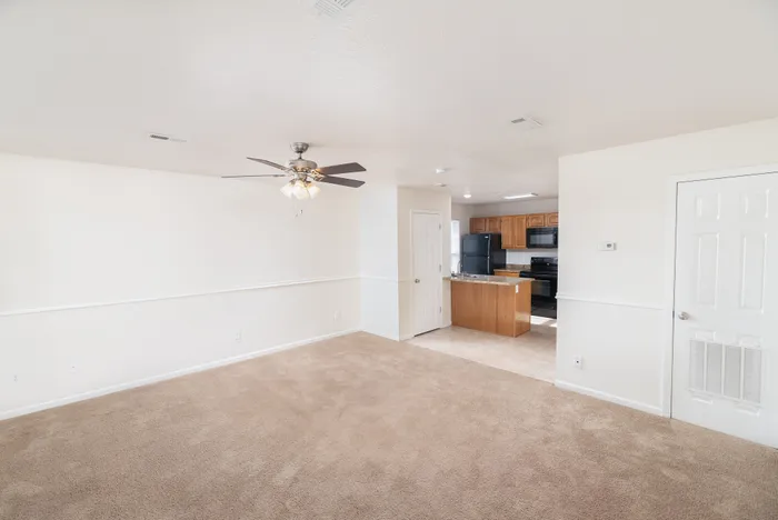 Inviting open-concept living area with plush carpet, sleek ceiling fan, and a modern kitchen featuring wood cabinetry and black appliances.