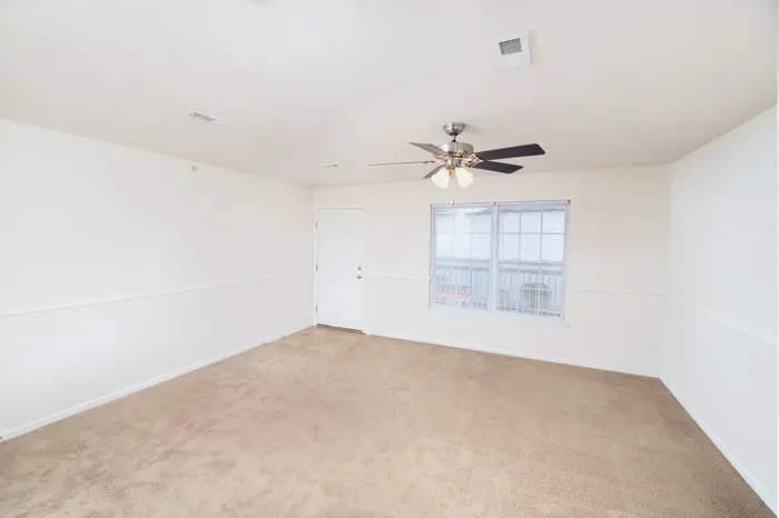 Bright and airy living room with plush carpet, ceiling fan, and large windows for natural light.