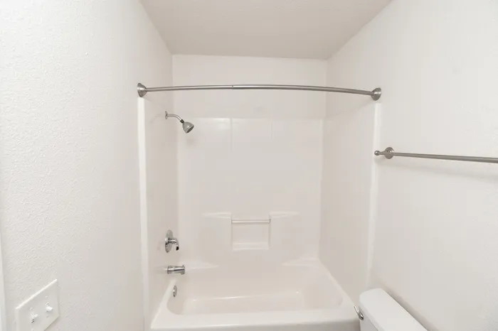 Bright and modern bathroom featuring a pristine white bathtub with a sleek chrome showerhead, creating a clean and inviting space.