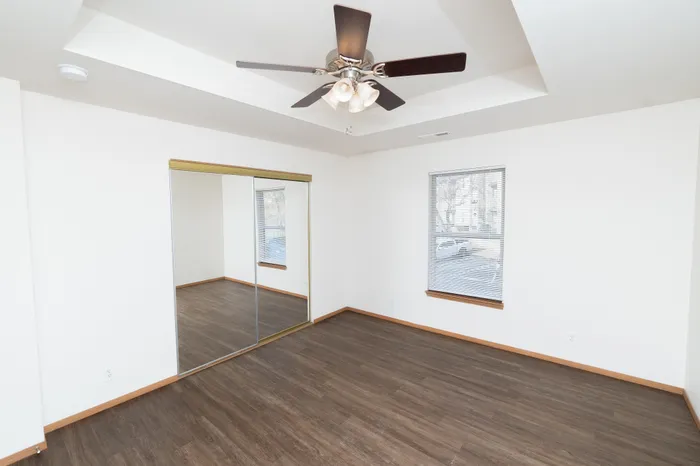 Bright and airy room with sleek hardwood floors, mirrored closet doors, and a stylish ceiling fan.