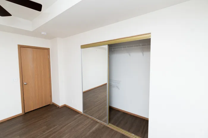 Modern room with sleek hardwood floors, mirrored sliding closet doors, and a clean, minimalist design.